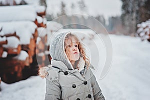Child girl in grey coat on the walk in snowy forest with tree felling