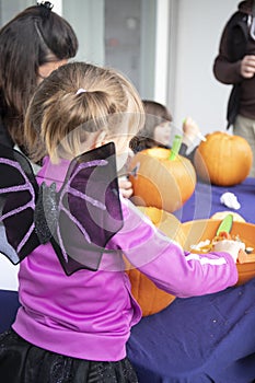 Child girl in halloween bat costume, carving pumpkins on Halloween day