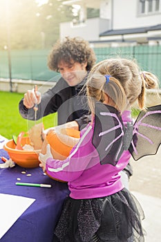 Child girl in halloween bat costume, carving pumpkins on Halloween day with her father