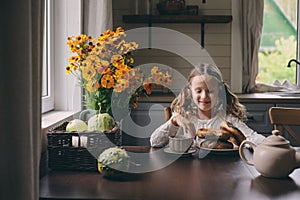 Child girl having breakfast at home in autumn morning. Real life cozy modern interior in country house