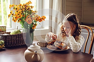 Child girl having breakfast at home in autumn morning. Real life cozy modern interior in country house