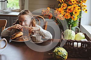 Child girl having breakfast at home in autumn morning. Real life cozy modern interior in country house