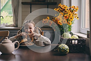 Child girl having breakfast at home in autumn morning. Real life cozy modern interior in country house