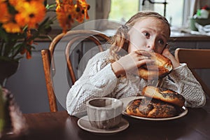 Child girl having breakfast at home in autumn morning. Real life cozy modern interior in country house