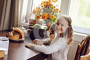 Child girl having breakfast at home in autumn morning. Real life cozy modern interior in country house