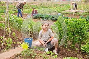 Child girl helping her parents work in vegetable garden