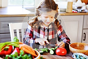 Child girl helps mom to cook and cut fresh vegetables for salad with knife