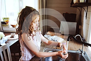 Child girl helps mother at home and wash dishes in kitchen