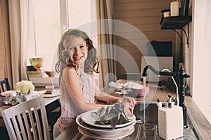 Child girl helps mother at home and wash dishes in kitchen