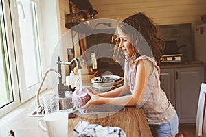 Child girl helps mother at home and wash dishes in kitchen. Casual lifestyle in real interior