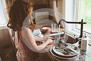 Child girl helps mother at home and wash dishes in kitchen. Casual lifestyle in real interior