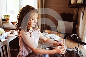 Child girl helps mother at home and wash dishes in kitchen. Casual lifestyle in real interior