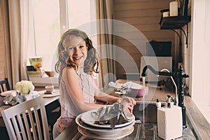 Child girl helps mother at home and wash dishes in kitchen photo