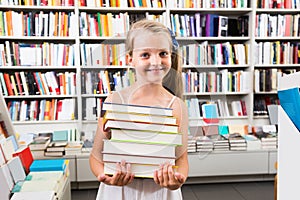 Child girl holding a stack of books in a bookstore