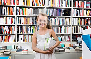 Child girl holding a stack of books in a bookstore