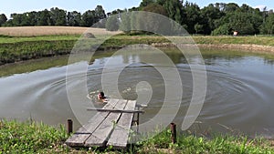 Child girl jump to pond water from wooden bridge and swim