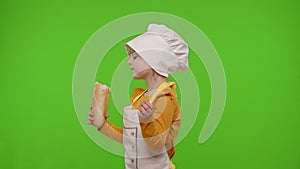 Child girl kid dressed in apron and hat like chef cook eating fresh tasty baguette, making faces