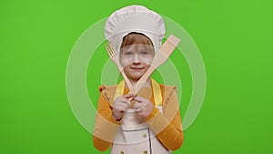 Child girl kid dressed as cook chef with fork and spatula, showing symbol of rejection, disagreement