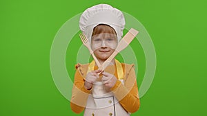 Child girl kid dressed as cook chef with fork and spatula, showing symbol of rejection, disagreement