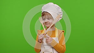 Child girl kid dressed as cook chef with fork and spatula, showing symbol of rejection, disagreement