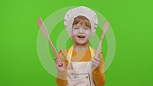 Child girl kid dressed as cook chef showing wooden fork and spatula, smiling, dancing on chroma key