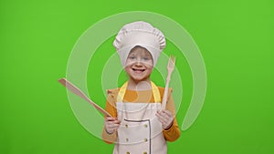 Child girl kid dressed as cook chef showing wooden fork and spatula, smiling, nods head in agreement