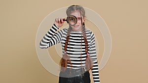 Child girl kid holds magnifying glass near face looking at camera with big zoomed eye, analyzing