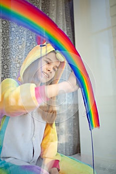 Child girl in kigurumi draws rainbow on window. photo