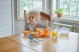 The child girl in the kitchen cuts and squeezes oranges juice