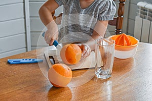 The child girl in the kitchen cuts and squeezes oranges juice