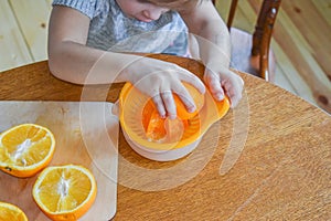 The child girl in the kitchen cuts and squeezes oranges juice