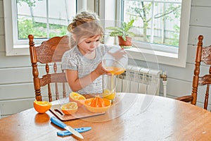 The child girl in the kitchen cuts and squeezes oranges juice
