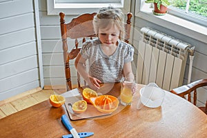 The child girl in the kitchen cuts and squeezes oranges juice