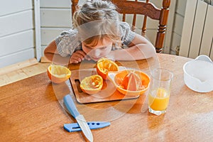 The child girl in the kitchen cuts and squeezes oranges juice
