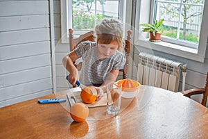 The child girl in the kitchen cuts and squeezes oranges juice