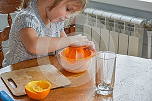 The child girl in the kitchen cuts and squeezes oranges juice