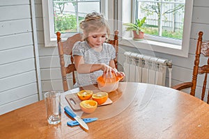 The child girl in the kitchen cuts and squeezes oranges juice