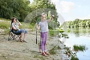 Child girl look on caught fish, people camping and fishing, family active in nature, river and forest, summer season