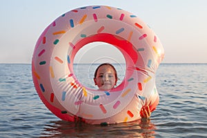 Child girl looking through pink donut inflatable lifebuoy