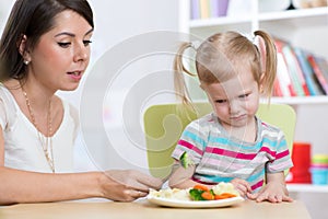 Child girl looks with disgust at healthy vegetables. Mother convinces her daughter to eat food.