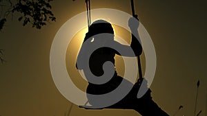 A child girl loves to swing and fly on a swing on summer evening on a playground. The girl is swinging on a swing in the