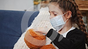 child girl in medical covid -19 protective mask play a teddy bear stay home. pandemic coronavirus concept. girl kid face