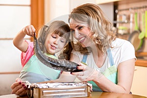 Child girl with mother cooking fish in the kitchen