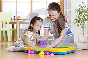 Child girl and mother playing with building toy sand at home