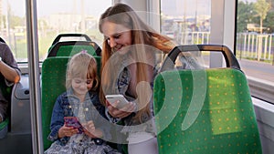 Child girl with mother using mobile phone internet social network application while traveling by bus