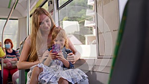 Child girl with mother using mobile phone internet social network application while traveling by bus