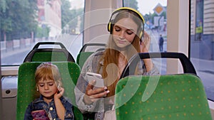 Child girl with mother using smartphone with headphones, earphones listening music, funny dancing