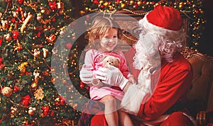 child girl in nightgown sitting on lap of Santa Claus around Christmas tree
