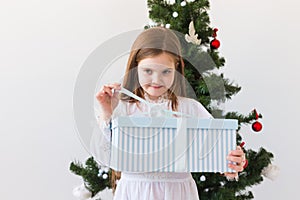 Child girl opens gift box near Christmas tree. Holidays, christmas time and presents concept.