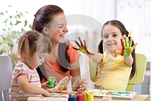 Child girl with painted hands. Kids drawing and coloring with teacher in daycare center.